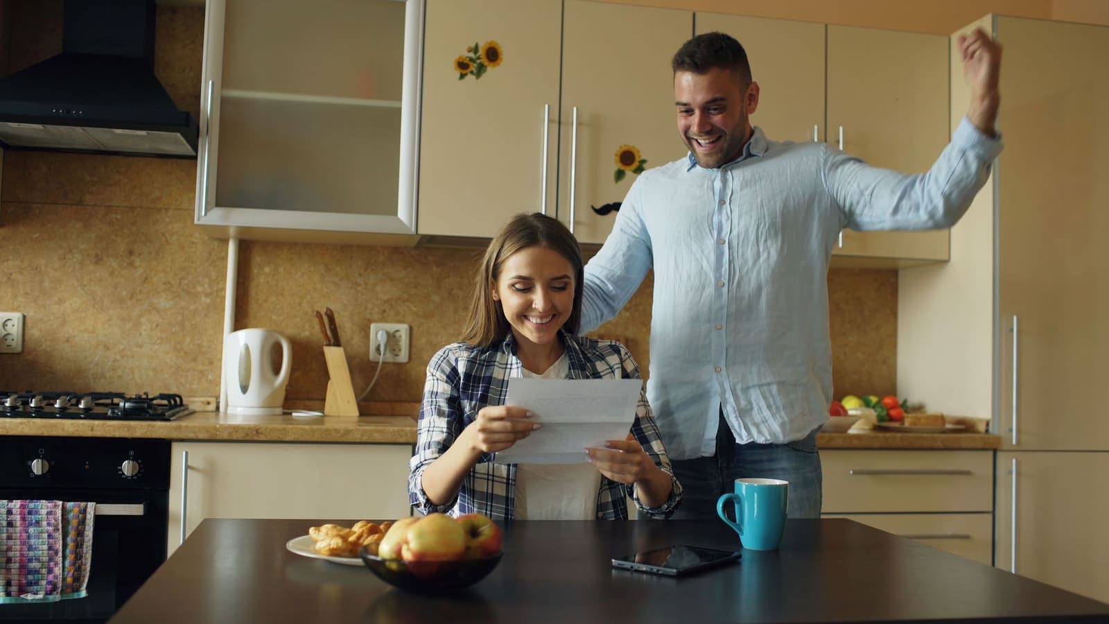 A couple in their kitchen reacting to good news that arrived by mail